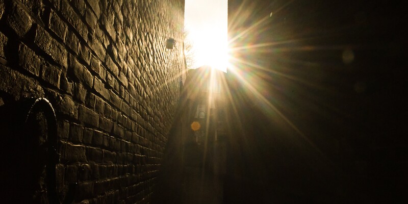 Gleißendes Licht strahlt von oben in eine Lücke zwischen zwei Gebäuden herein.