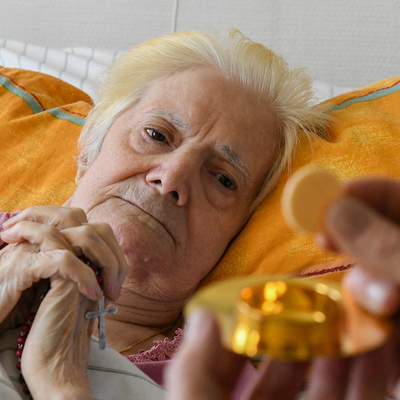 Eine Frau hat die Hände zum Gebet gefaltet und schaut auf die Hostienschale während der Krankenkommunion auf der Palliativstation in der Universitätsklinik Bonn am 12. März 2021.