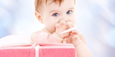 Baby mit Geschenk / © stock.adobe.com/Syda Productions Baby staunt über ein noch verpacktes Geschenk