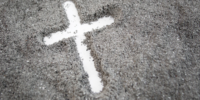 mit Finger gezeichnetes weißes Kreuz auf grauem Asche-Hintergrund