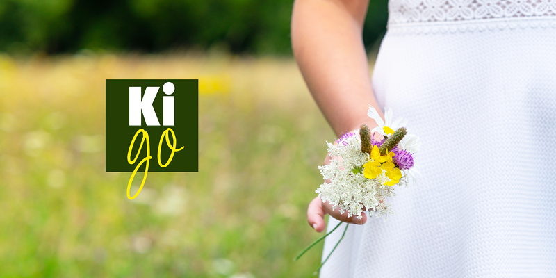 Ein Kind in weissem Kleid mit einem Wildblumenstrauss.