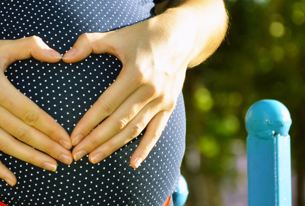 Hände formen ein Herz auf dem Bauch einer schwangeren Frau.